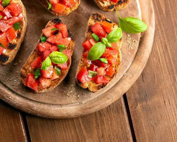 Bruschette veloci per aperitivo: fette di pane tostato con pomodoro fresco a cubetti e basilico, pronte per essere gustate.