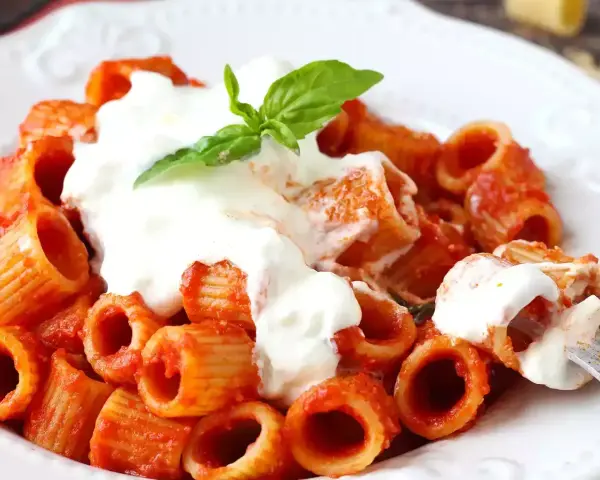 Rigatoni al sugo con abbondante stracciatella cremosa e una fogliolina di basilico fresco.