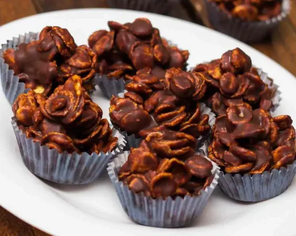 Deliziosi biscotti corn flakes e cioccolato, croccanti e golosi, serviti in pirottini argentati su un piatto bianco.