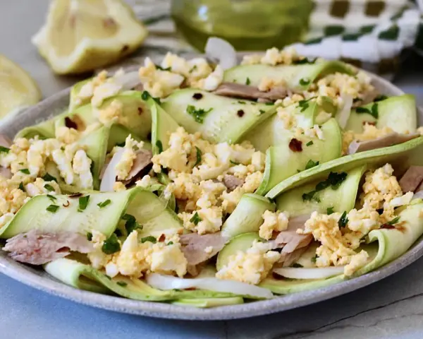 Deliziosa insalata di zucchine crude a nastro, condita con tonno, uova sode sbriciolate e prezzemolo fresco.