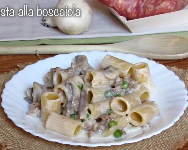 Piatto di pasta alla boscaiola con funghi, piselli e salsiccia, servita su un piatto bianco bordato.