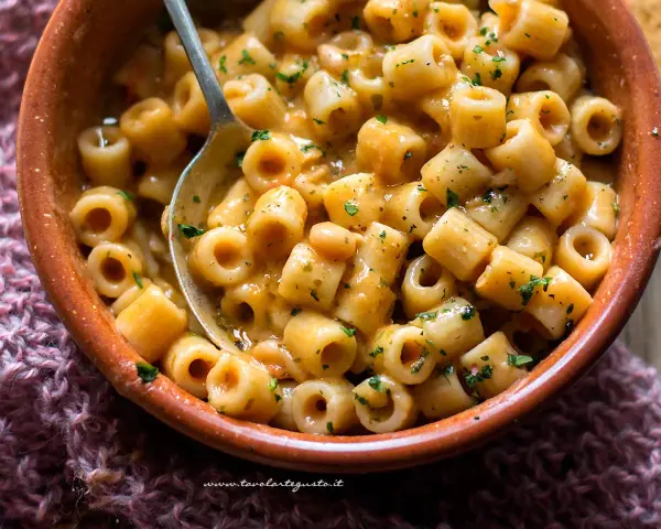 Un piatto invitante di pasta e fagioli estiva, condita con erbe fresche, servita in una ciotola di terracotta.