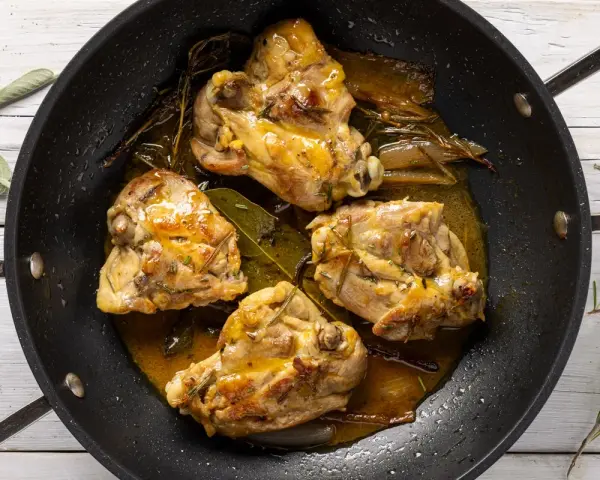 Cosce di pollo in padella, dorate e succulente, con erbe aromatiche e un sughetto invitante.