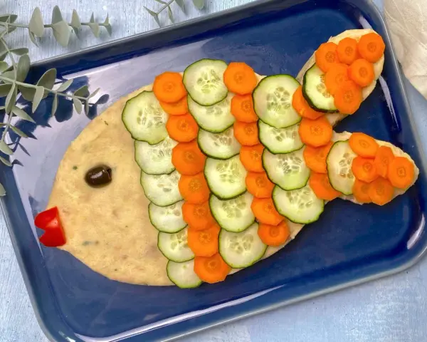 Un simpatico pesce finto ricetta, con corpo di purè, scaglie di cetriolo e carota, occhio d'oliva e bocca di peperone rosso.