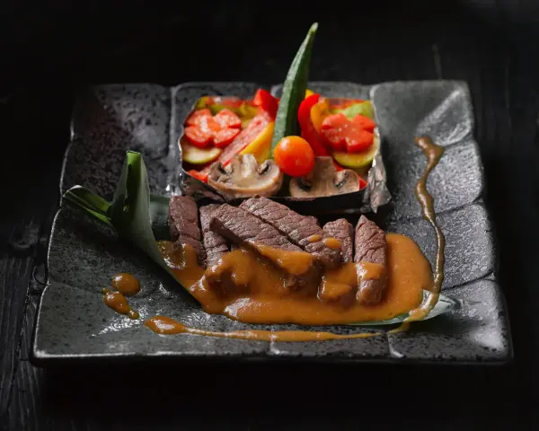 Straccetti di manzo succulenti su un piatto scuro, accompagnati da verdure miste e una salsa cremosa.