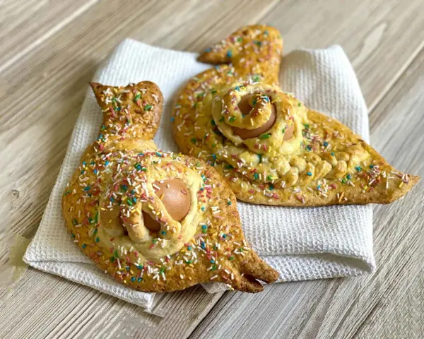 Due cuddure cu l'ova, dolci pasquali decorati con zuccherini colorati, riposano su un panno bianco.