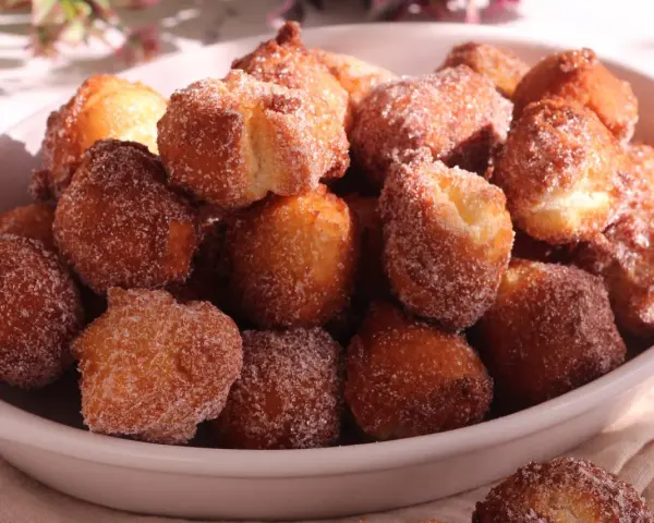 Un piatto colmo di castagnole ricetta della nonna, dorate e cosparse di zucchero. Un dolce che sa di casa e tradizione.