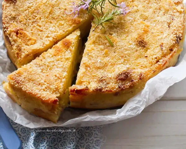 Gateau di patate alla siciliana dorato e croccante, guarnito con rosmarino fresco. Una fetta è già stata servita.