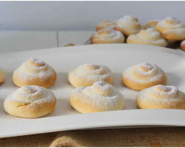 Biscotti a spirale cosparsi di zucchero a velo, perfetti con una tazza di caffè o tè, magari preparati con un tocco di latte condensato.