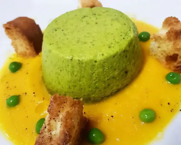 Sformato di piselli verde brillante su crema gialla, guarnito con piselli freschi e crostini dorati.
