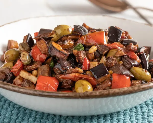 Caponata ricetta: melanzane, peperoni, olive e capperi in un piatto invitante.