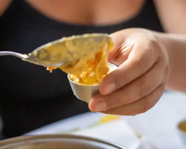 Una mano versa un cucchiaio di budino di riso in una coppetta.