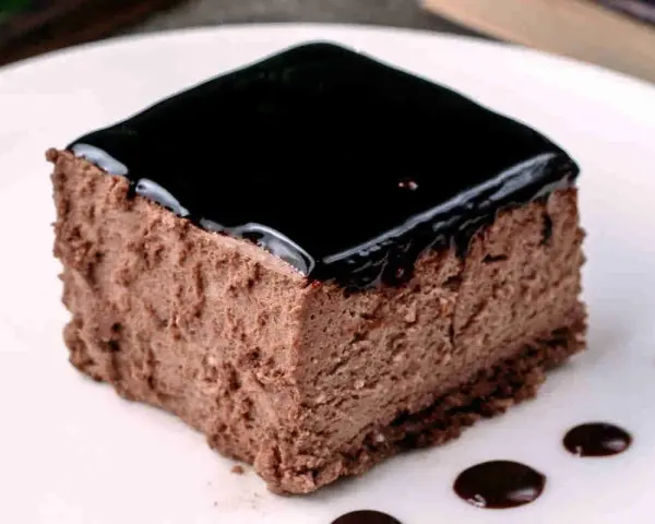 Un delizioso semifreddo al cioccolato, con una lucida glassa scura e gocce di salsa al cioccolato sul piatto bianco.