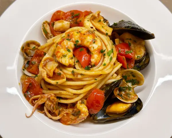Un piatto invitante di spaghetti allo scoglio, con gamberi, cozze, vongole e calamari, condito con pomodorini freschi e prezzemolo.