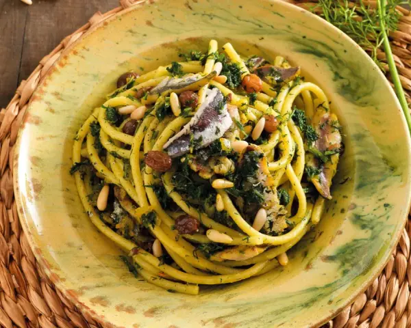 Un piatto di pasta con le sarde, condita con finocchietto selvatico, pinoli e uvetta, servita in un piatto decorato.