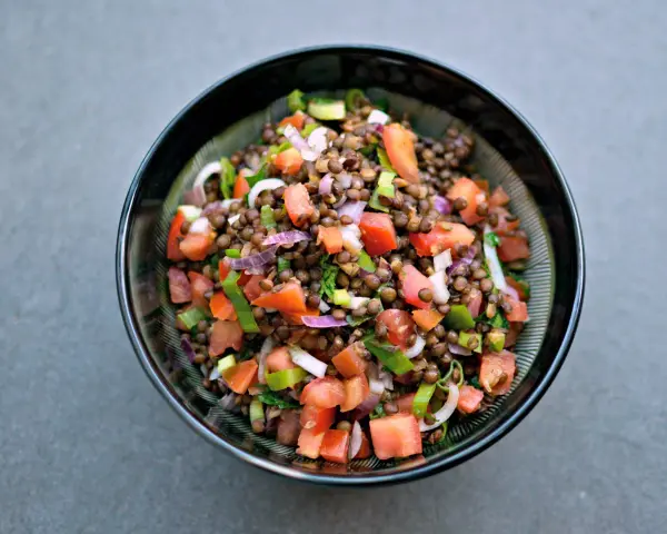 Una ciotola di insalata di lenticchie colorata con pomodori, cipolla rossa e erbe fresche.