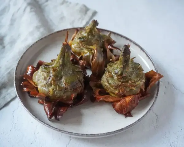Tre carciofi alla giudia dorati e croccanti su un piatto, pronti per essere gustati.
