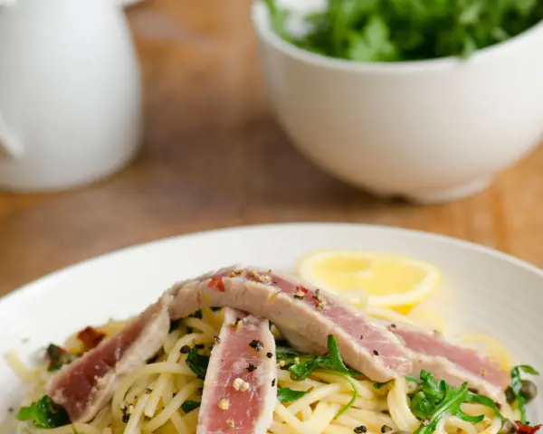 Spaghetti con tonno fresco alla siciliana, guarniti con rucola, capperi, pomodori secchi e una fetta di limone.