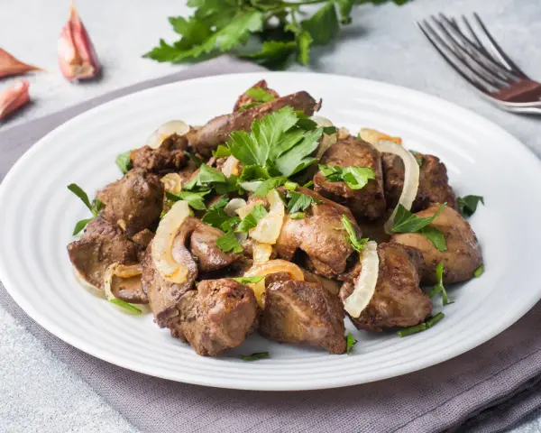 Piatto di fegato alla veneziana con cipolle e prezzemolo, contornato da aglio e pepe.