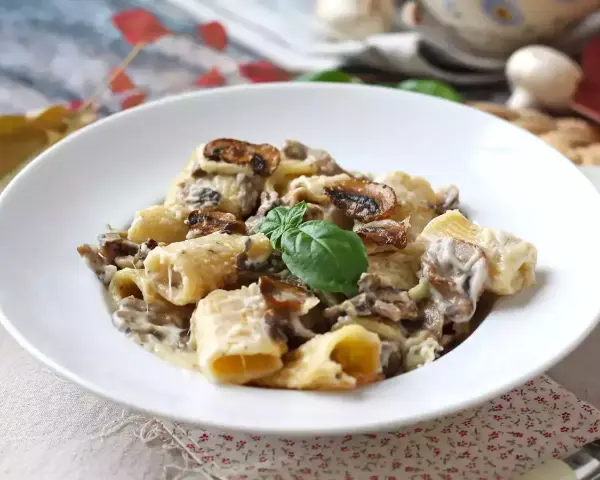 Un piatto invitante di pasta funghi e panna, con rigatoni conditi generosamente e guarniti con basilico fresco.