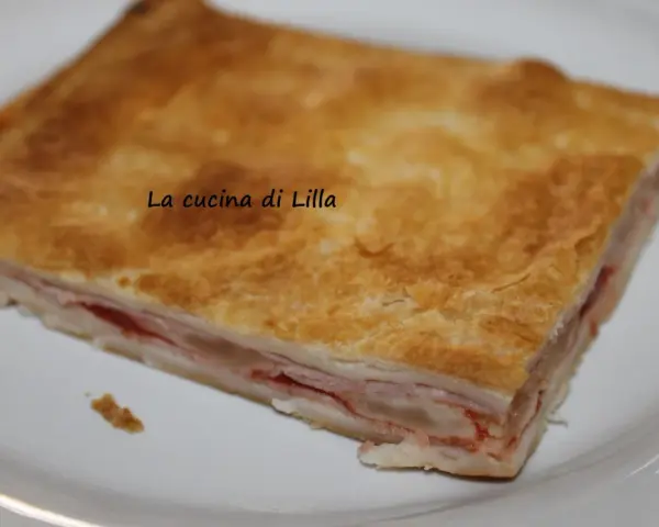 Una fetta di torta salata prosciutto e formaggio, con pasta sfoglia dorata e ripieno filante.