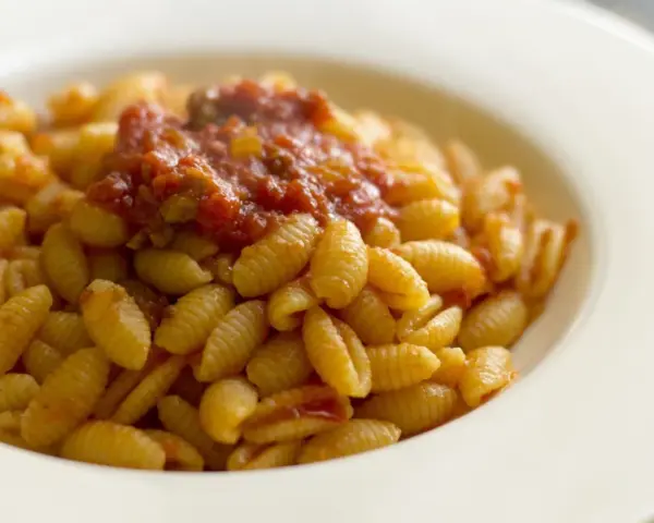 Malloreddus alla campidanese, pasta sarda con sugo di pomodoro e salsiccia, serviti in un piatto bianco.
