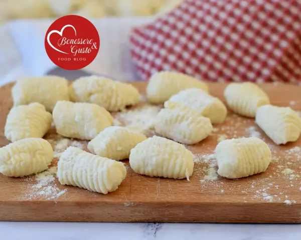 Gnocchi di ricotta freschi, pronti per essere cucinati, spolverati di farina su un tagliere di legno.