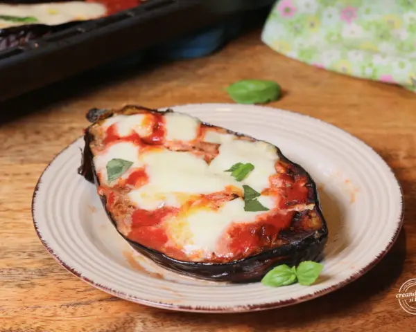 Melanzane alla pizzaiola appena sfornate, con mozzarella filante e basilico fresco su un piatto rustico.