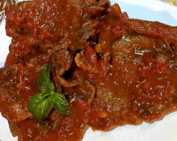 Fette di carne alla pizzaiola, ricoperte da un sugo rosso saporito e guarnite con basilico fresco.