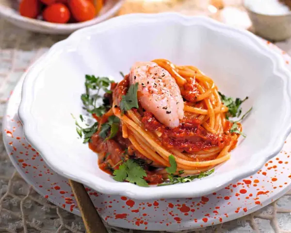Spaghetti con gamberetti e pomodorini alla siciliana, un piatto colorato e saporito, guarnito con prezzemolo fresco.