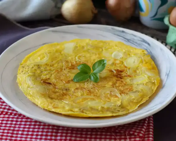 Una dorata frittata di cipolle, guarnita con basilico fresco, servita su un piatto bianco.