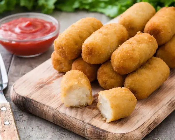 Crocchette di patate dorate e croccanti, servite su un tagliere di legno con ketchup e una forchetta.