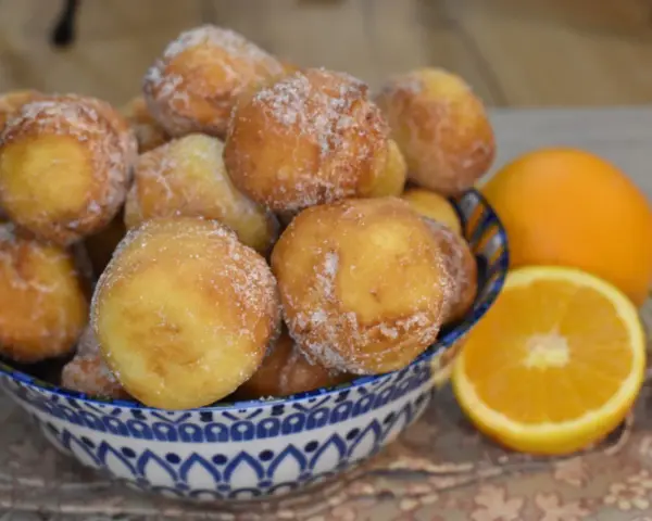 Arancini dolci, soffici arrubiolus di ricotta cosparsi di zucchero, accanto a fette d'arancia.
