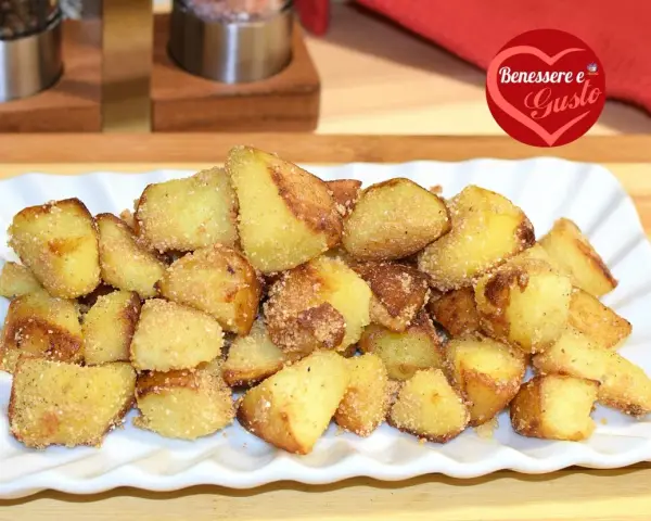 Patate sabbiose in padella, dorate e croccanti, servite su un piatto bianco. Un contorno irresistibile.
