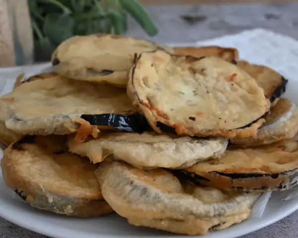 Piatto di melanzane fritte pastellate, dorate e croccanti, pronte per essere gustate.