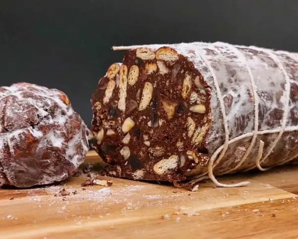 Salame al cioccolato vegano, un dolce goloso con biscotti e frutta secca, spolverato di zucchero a velo.