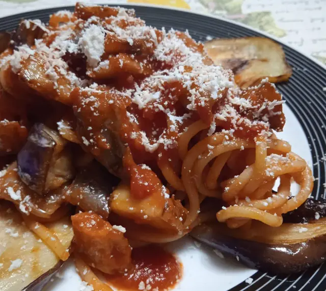 Un piatto invitante di pasta alla norma con melanzane fritte, sugo di pomodoro e ricotta salata grattugiata.