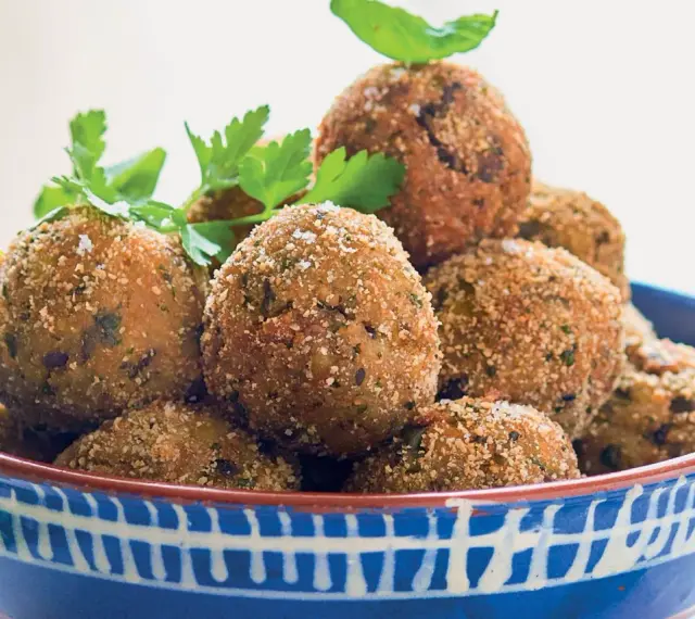 Polpette di melanzane dorate e croccanti, guarnite con prezzemolo fresco, in una ciotola blu decorata.