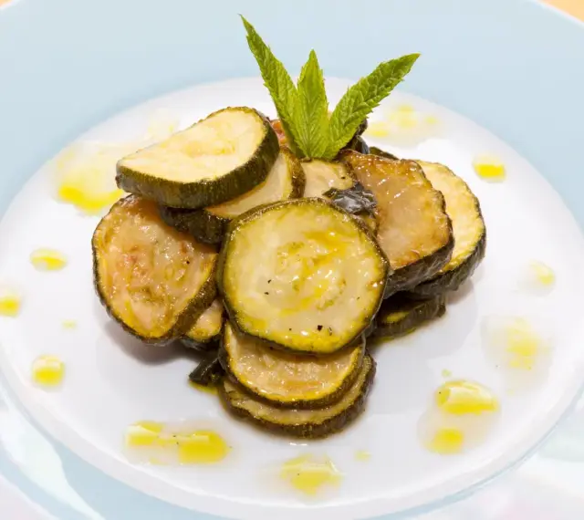 Fette di zucchine alla scapece, condite con olio e guarnite con menta fresca, su un piatto bianco.