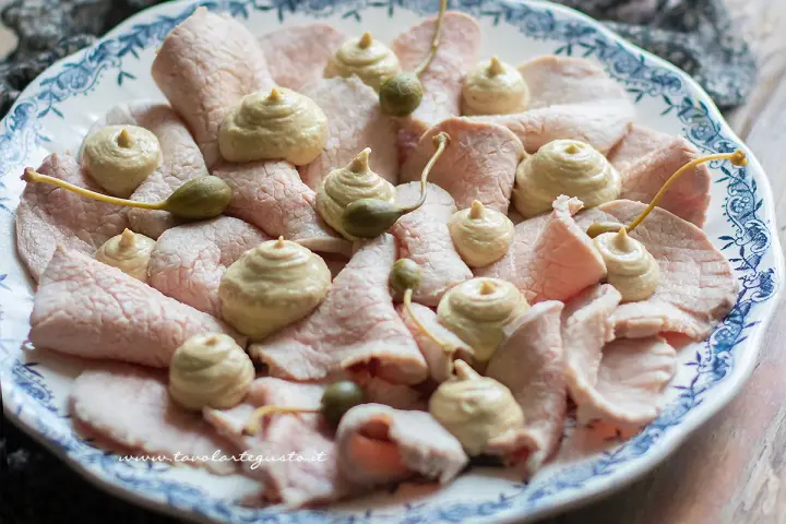 Piatto di vitello tonnato con salsa cremosa, capperi e guarnizioni.