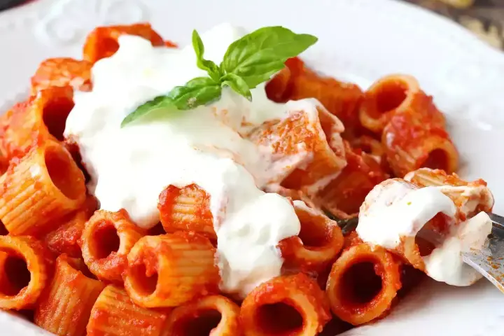Rigatoni al sugo con abbondante stracciatella cremosa e una fogliolina di basilico fresco.