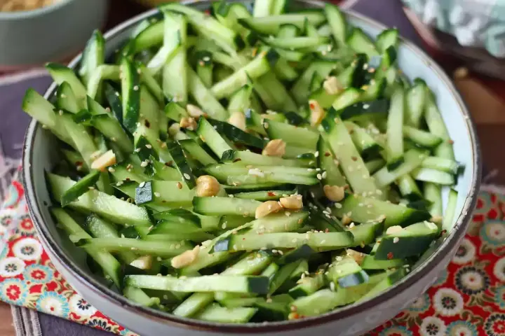 Una ciotola piena di fresca insalata di cetrioli tagliati a julienne, condita con semi di sesamo e arachidi croccanti.