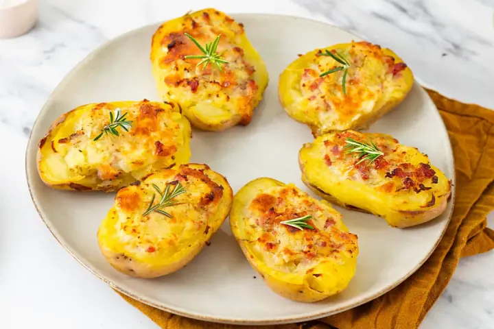 Patate ripiene al forno, dorate e gratinate, guarnite con rosmarino fresco. Un piatto invitante e saporito.