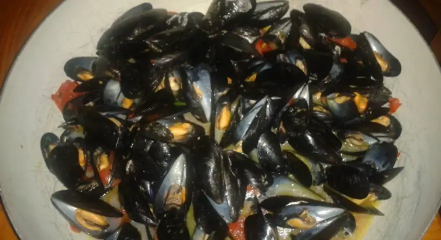 Un'abbondante impepata di cozze in un piatto largo, con pomodorini e un sughetto invitante.