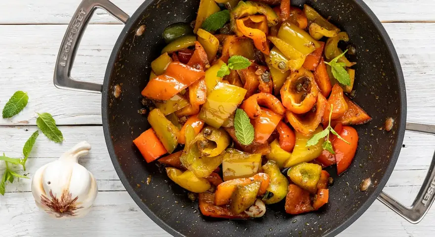 Peperoni in padella, colorati e succosi, con foglie di menta fresca e uno spicchio d'aglio.