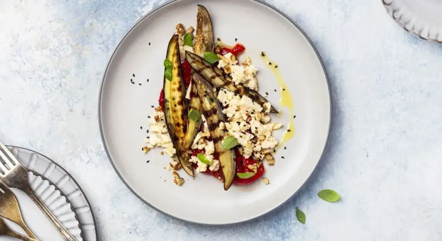 Deliziosa insalata di melanzane grigliate con feta sbriciolata, pomodoro, noci e semi di sesamo nero, condita con olio d'oliva.