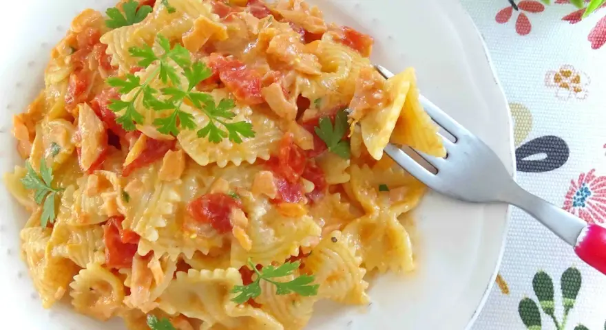 Farfalle cremose con pomodorini e salmone, guarnite con prezzemolo fresco. Un piatto invitante pronto per essere gustato.