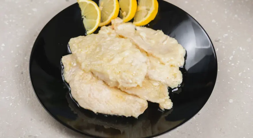 Scaloppine di pollo al limone, un piatto classico e saporito, servite su un piatto nero con spicchi di limone fresco.