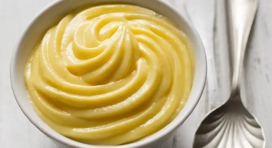 Una ciotola di soffice crema pasticcera, pronta per essere gustata. Accanto, un cucchiaio d'argento.