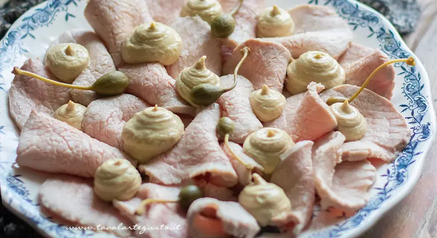 Piatto di vitello tonnato con salsa cremosa, capperi e guarnizioni.